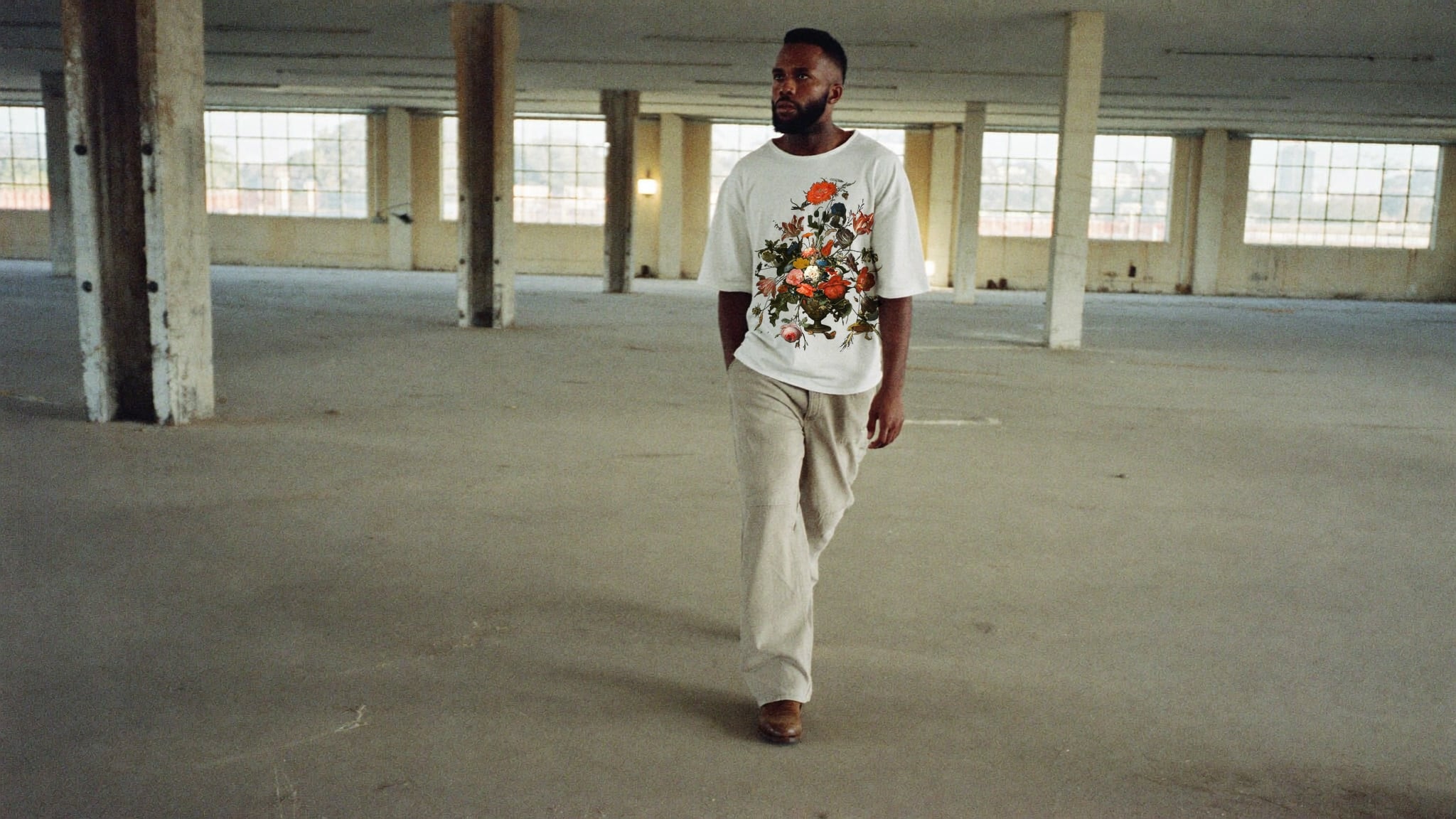 Off-white heavyweight tee with the Floral Still Life print, a painted bouquet of red and white flowers, worn with stone trousers