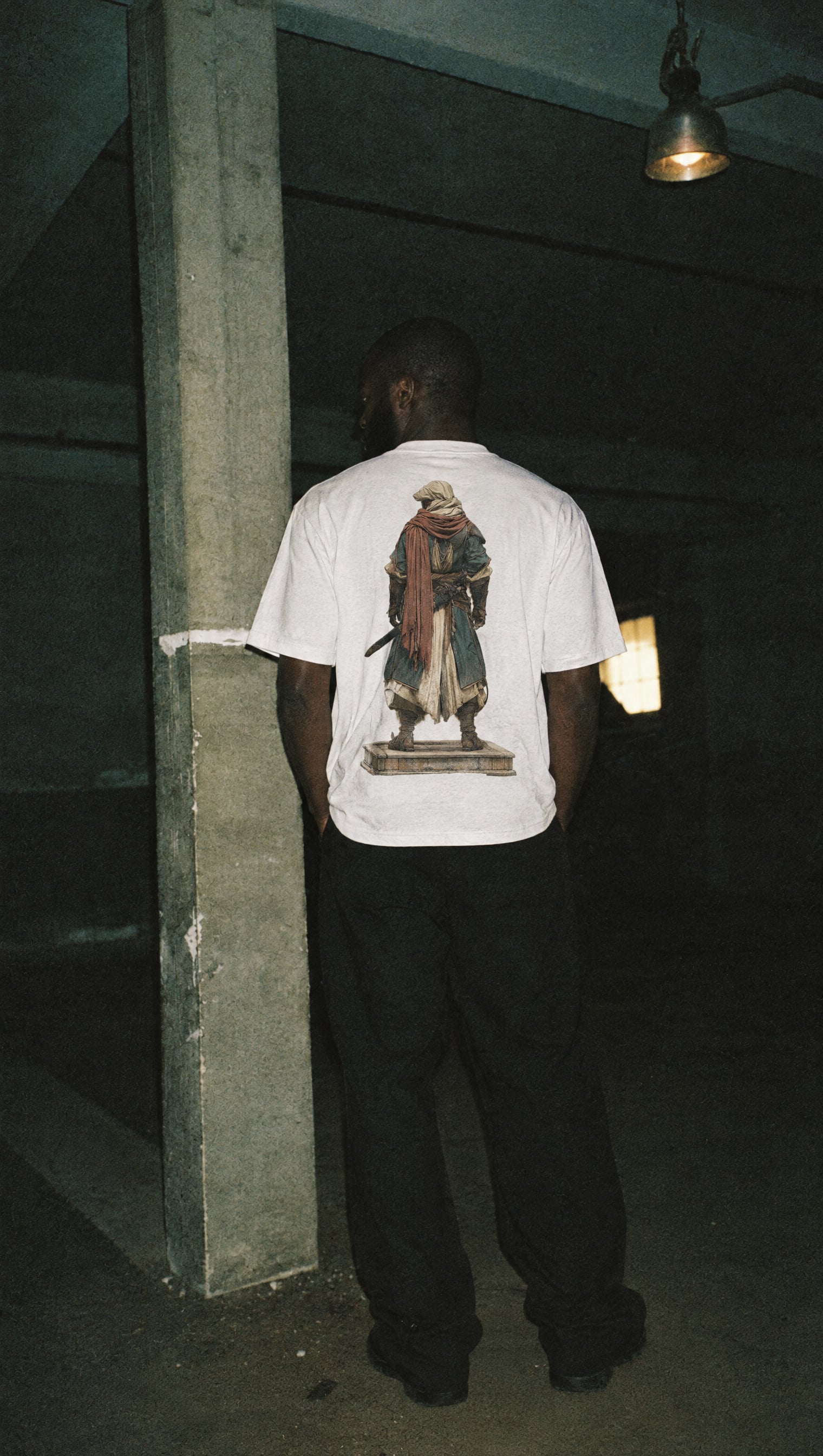 White heavyweight tee with the Warrior back print: a robed figure with a red scarf standing on a stone plinth